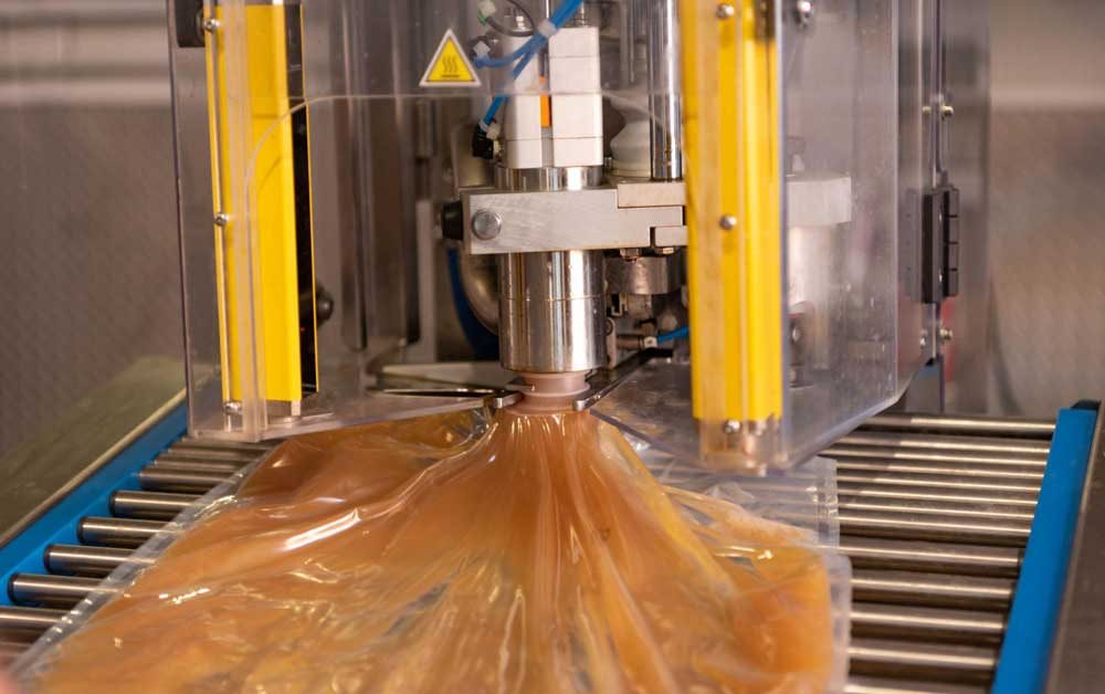 Flexible bag beneath an industrial filling head on a roller conveyor
